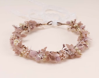 May include: A delicate floral crown made with dried flowers in shades of pink and white. The crown is made with a wire base and is adorned with small, delicate flowers and leaves.