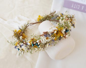 May include: A floral crown made of dried flowers in shades of white, yellow, and blue. The crown is made on a wire base and is perfect for a wedding or special occasion.