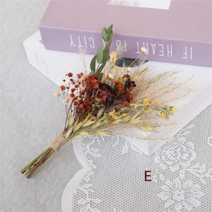 May include: A small bouquet of dried flowers in shades of brown, yellow, and white. The bouquet is tied with twine and includes dried grasses, small white flowers, and a few larger brown flowers.