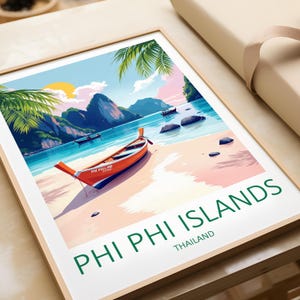 May include: A framed art print depicting a beach scene from Phi Phi Islands, Thailand. The artwork shows an orange longtail boat on a sandy shore, with turquoise water, green mountains, and a setting sun. The text "PHI PHI ISLANDS" is printed in green.