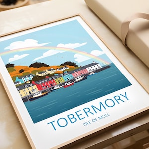 Può includere: Una stampa artistica incorniciata con un'illustrazione colorata di Tobermory, Isola di Mull. L'opera raffigura una fila di edifici dai colori vivaci lungo un porto, con barche, un arcobaleno e il testo "TOBERMORY" e "ISLE OF MULL". La stampa è in una cornice di legno.
