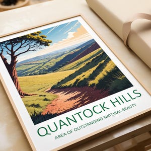 May include: A framed print of a landscape scene with rolling green hills and a winding path. The print features a blue sky with white clouds and a single tree in the foreground. The text "Quantock Hills Area of Outstanding Natural Beauty" is printed in green at the bottom of the print.