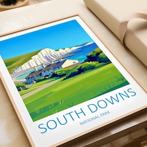 Peut inclure: Une affiche encadrée représentant une illustration du parc national de South Downs. L'œuvre d'art dépeint un paysage côtier avec des falaises blanches, des collines vertes, la mer bleue et un ciel clair. Les mots "SOUTH DOWNS NATIONAL PARK" sont imprimés en bas.