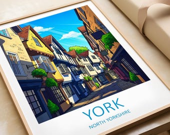 May include: Framed art print featuring a stylized illustration of a street scene in York, North Yorkshire. The artwork depicts colorful buildings with detailed architectural features under a bright blue sky. The word "YORK" is printed in blue.