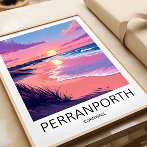 May include: A framed art print depicting a sunset over Perranporth beach in Cornwall. The image shows a colorful sky with pink and purple clouds, reflecting on the sea. The text "PERRANPORTH CORNWALL" is printed at the bottom of the print.