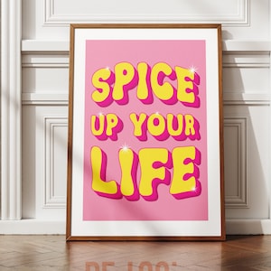 May include: A pink poster with the text "Spice Up Your Life" in yellow 3D letters with a pink outline. The letters have a glossy finish and sparkle.