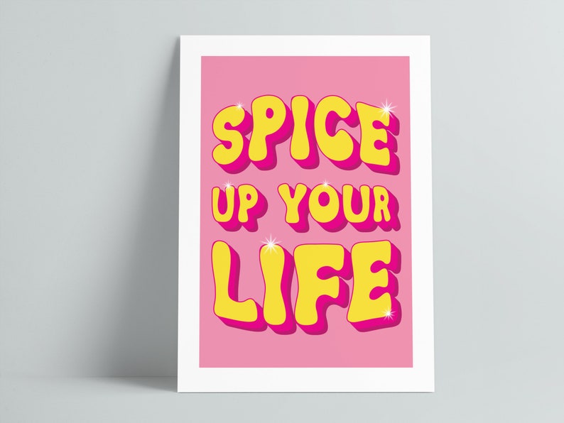 May include: Pink background with the text "Spice Up Your Life" in yellow letters with a pink outline. The letters are in a retro, bubbly font.