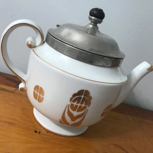 May include: White porcelain teapot with a silver lid and a black knob. The teapot has a gold floral design.