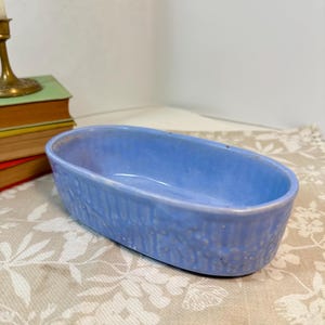 Könnte beinhalten: Eine ovale Keramikschale mit hellblauer Glasur. Die Außenseite der Schale weist ein strukturiertes, vertikales Rippenmuster auf, das sich um den gesamten Umfang erstreckt. Das Innere ist glatt und konkav mit einer gleichmäßigen blauen Farbe.