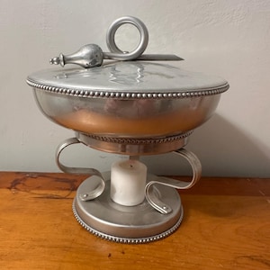 Peut inclure: Un plat à réchaud en métal argenté avec un couvercle et une poignée. Le plat repose sur un support avec des supports incurvés et une base. Une bougie blanche est à l'intérieur du support. Le couvercle a un bouton décoratif.