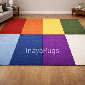 Könnte beinhalten: Ein farbenfroher Teppich mit Regenbogenmuster. Der Teppich ist in acht rechteckige Abschnitte unterteilt, die jeweils eine andere Farbe haben: rot, orange, gelb, grün, blau, lila und weiß. Der Text "InayaRugs" ist auf dem Teppich sichtbar.