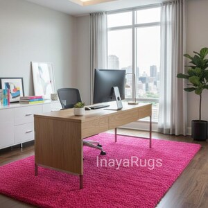 May include: A modern office space featuring a vibrant pink shag rug. The room includes a wooden desk, a black office chair, and a large window with city views. The rug covers most of the floor space.