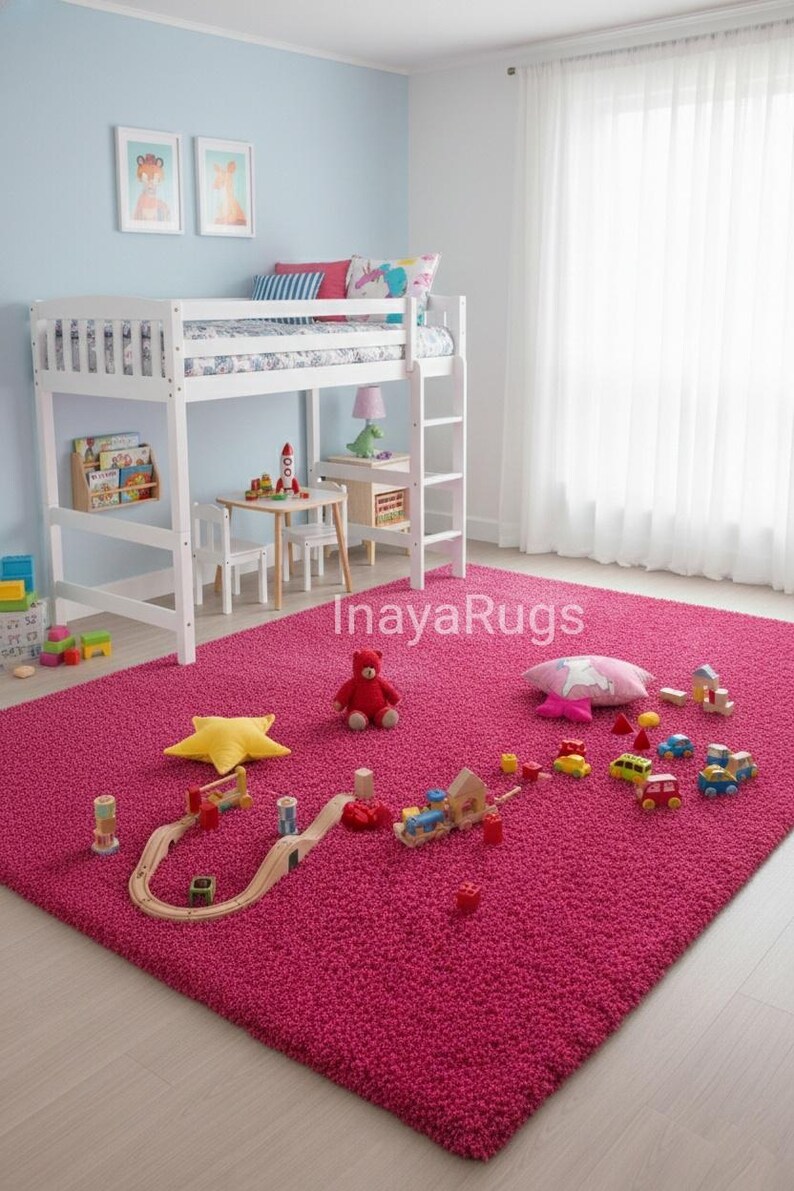 May include: A bright pink shag rug fills a child's bedroom, with a white bunk bed, small table, and toys scattered across it. A wooden train track, toy cars, and a teddy bear are visible.
