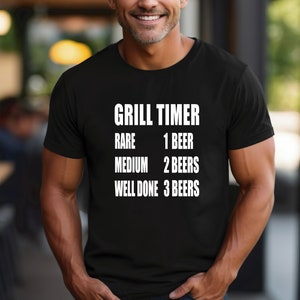 May include: Black t-shirt with white text that reads "Grill Timer" and a list of doneness levels for meat with corresponding beer counts: "Rare 1 Beer", "Medium 2 Beers", "Well Done 3 Beers".