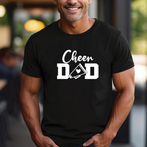 May include: Black t-shirt with white text that reads "Cheer Dad" and a white megaphone with a heart.