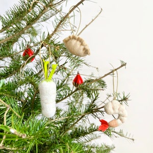 Könnte beinhalten: Ein Weihnachtsbaum, der mit Filz-Anhängern in Form eines Knödels, einer Garnele und eines Rettichs geschmückt ist. Die Anhänger sind hellbeige mit roten Akzenten.