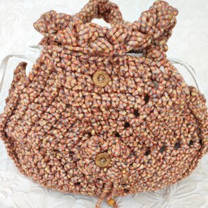 May include: A crocheted bag with a brown and orange striped pattern. The bag has two wooden buttons and a drawstring closure.