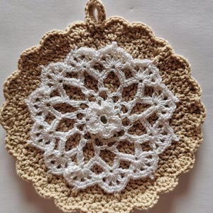 May include: A crocheted pot holder with a white centre and a tan outer edge. The pot holder has a loop for hanging.