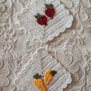 Puede incluir: Dos posavasos cuadrados blancos, de ganchillo, con bordes festoneados. Uno tiene dos aplicaciones de remolacha roja con copas verdes. El otro tiene dos aplicaciones de zanahoria amarilla con copas verdes. Los posavasos están sobre una superficie blanca texturizada.