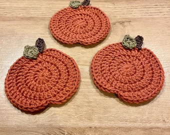 May include: Three crocheted pumpkin-shaped coasters in a burnt orange color with green and brown leaves.