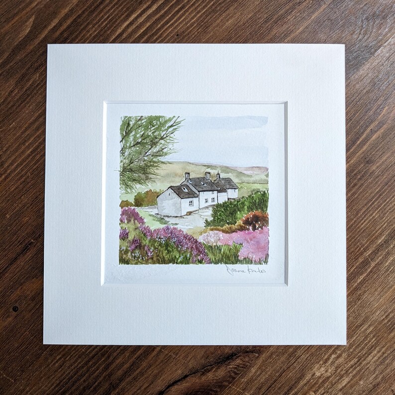 May include: A watercolor painting of a white cottage with a green roof, surrounded by purple flowers and green trees. The painting is signed "Joanne Kidd" in the bottom right corner.