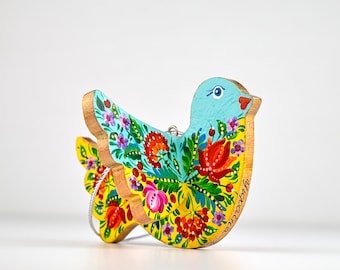 May include: A wooden bird ornament, hand-painted with a vibrant floral design. The bird features a light blue head, yellow body, and colorful flowers in red, pink, and green. The edges are outlined in gold. A decorative item.
