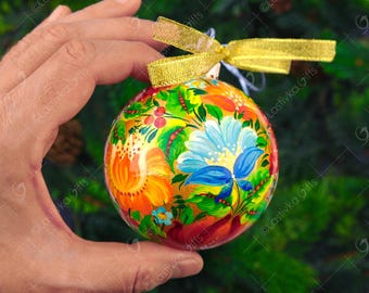 May include: A hand-painted Christmas bauble with a floral design in shades of red, orange, yellow, blue, and green. The bauble is round and has a gold ribbon attached to it.