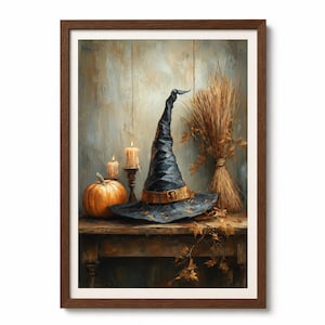 May include: A framed wall art print featuring a dark blue pointed witch hat with a tan buckle band, an orange pumpkin, two lit candles in dark holders, and a bundle of dried wheat stalks arranged on a wooden table against a textured backdrop.