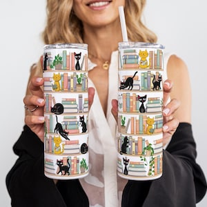 May include: Two stainless steel insulated tumblers with a whimsical design of bookshelves and cats. The cats are black and yellow, and the books are in various colors. One tumbler has a straw.