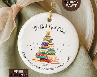 May include: A white ceramic Christmas ornament with a gold string. The ornament features the text "The Book Nook Club" and a Christmas tree made of books. The names Olivia, Sarah, Lily, Amanda, Henry, and Stella are also on the ornament. The year 2025 is also displayed.