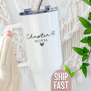 May include: White insulated tumbler with a handle, featuring the text "Chapter 40" and the name "Olivia" with a leopard print heart. The tumbler has a clear lid and a straw. The tumbler is held by a person wearing a cream-colored sweater.