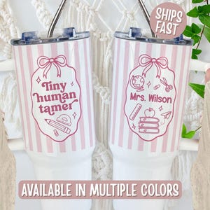 May include: Two white tumblers with pink vertical stripes and a pink design. One says "Tiny human tamer" with a pencil and ruler graphic. The other says "Mrs. Wilson" with school-themed graphics. The text "AVAILABLE IN MULTIPLE COLORS" is at the bottom.