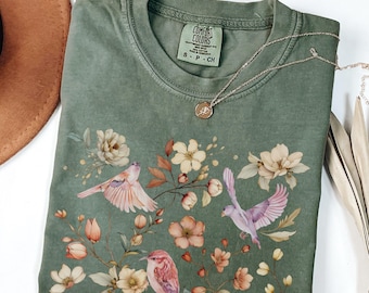 May include: A green t-shirt with a floral print and birds. The shirt has a tag that says "Comfort Colors" and "S - P - CH". The word "MOSS" is printed at the bottom of the image.