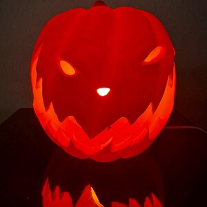 May include: A glowing orange jack-o'-lantern with a carved scary face. The pumpkin is lit from inside, creating a spooky effect.