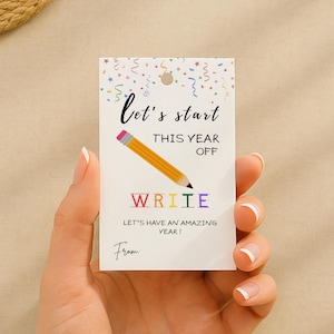 May include: A white gift tag with the text "let's start this year off" and "write" in colorful letters. A yellow pencil graphic is featured. The tag is held by a hand.