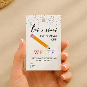 Peut inclure: Une étiquette rectangulaire blanche avec le texte "let's start this year off" et "write" en lettres colorées. Un crayon jaune est également présent. L'étiquette comprend la phrase "Let's have an amazing year together!" et un espace pour une signature.