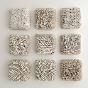May include: Nine square ceramic wall sculptures with different textured surfaces. The sculptures are all white and have a raised, textured surface. The textures include small circles, spikes, and small, rounded shapes.