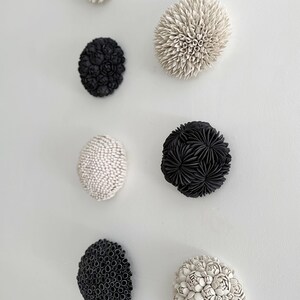 May include: A set of eight ceramic wall sculptures in black and white. The sculptures are round and have a textured surface. They are arranged in a vertical row on a white wall.