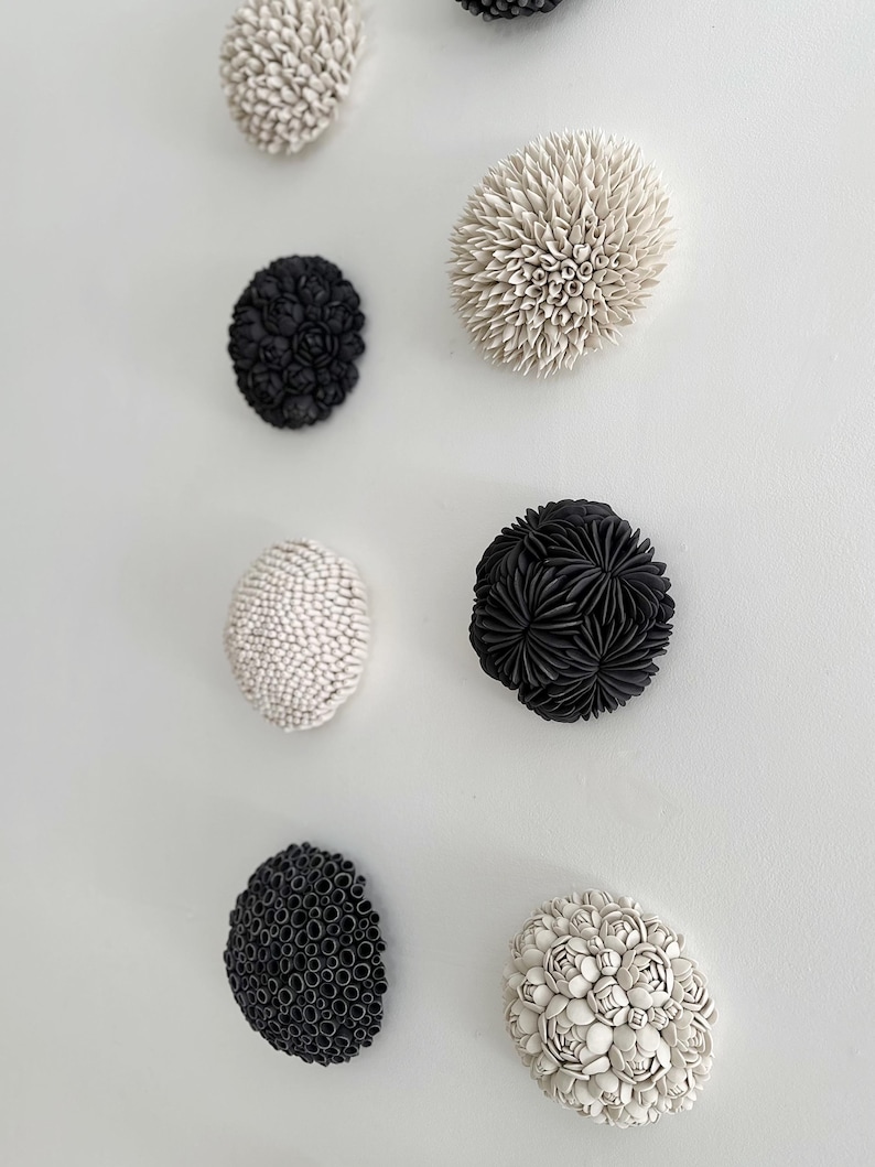 May include: A set of eight ceramic wall sculptures in black and white. The sculptures are round and have a textured surface. They are arranged in a vertical row on a white wall.