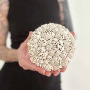 May include: A white ceramic sculpture of a flower bouquet, resembling a ball of small, rounded petals.