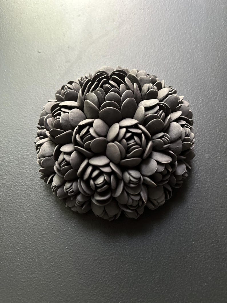 May include: A black ceramic sculpture of a flower with a round shape. The sculpture is made up of many small, overlapping petals.