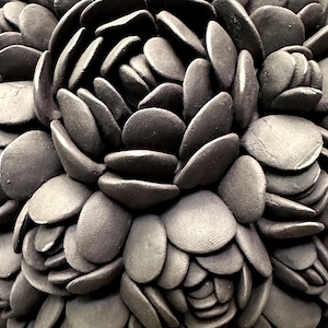 May include: Close-up of a black and gray ceramic flower sculpture. The flower is made up of many overlapping petals, creating a textured and organic look.