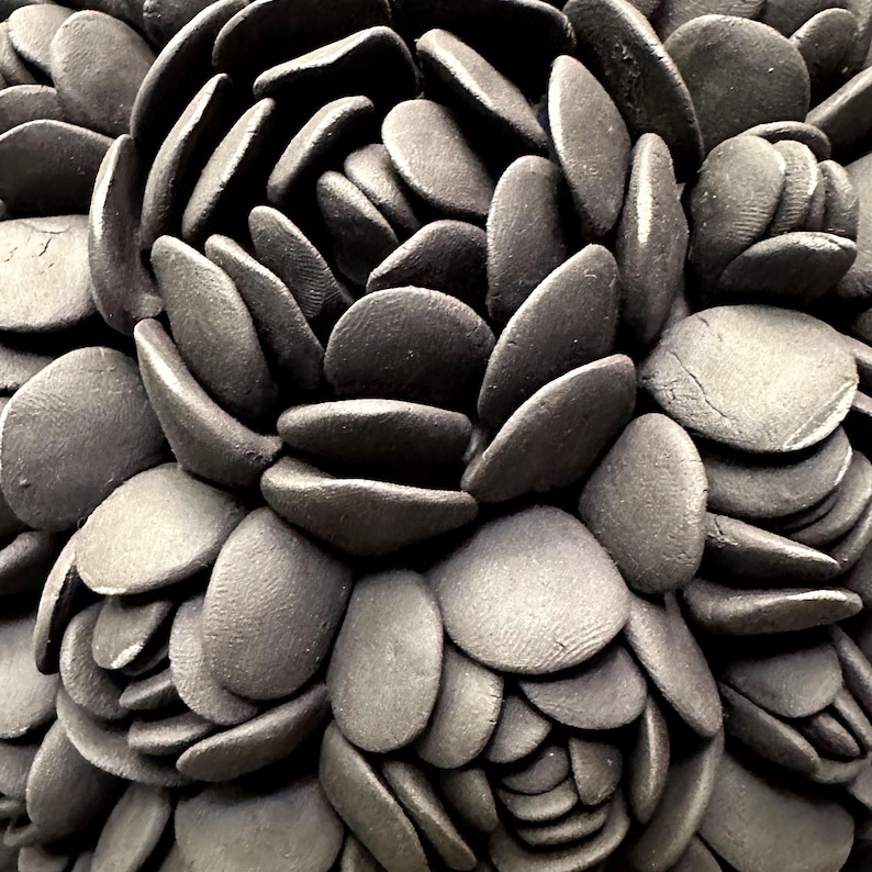 May include: Close-up of a black and gray ceramic flower sculpture. The flower is made up of many overlapping petals, creating a textured and organic look.