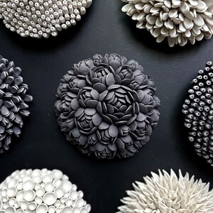 May include: Six ceramic wall sculptures in various shapes and sizes. The sculptures are all white or gray and have a textured surface. They are arranged in a circle on a black background.