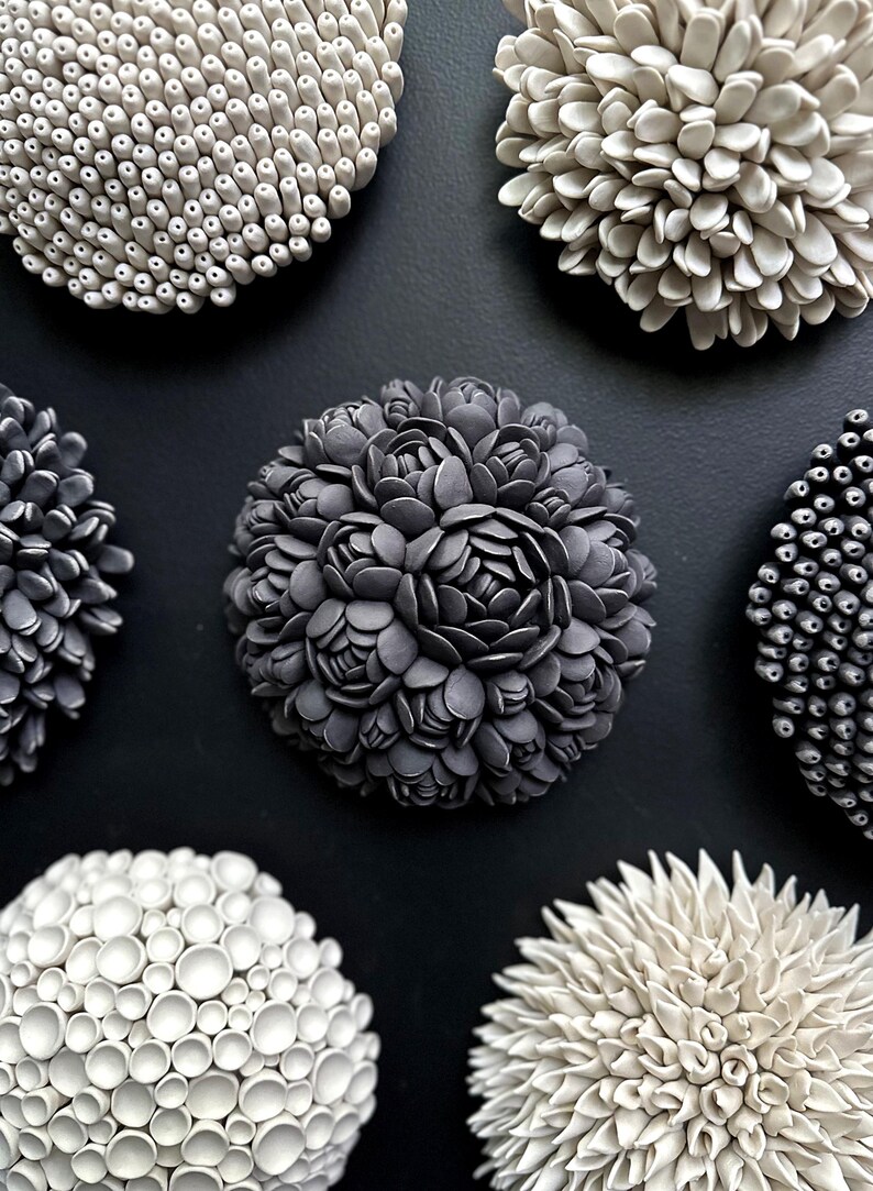 May include: Six ceramic wall sculptures in various shapes and sizes. The sculptures are all white or gray and have a textured surface. They are arranged in a circle on a black background.