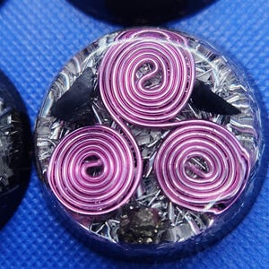 May include: A round, clear resin orb containing three pink wire spirals and two black crow figures. The orb is filled with silver and black glitter.