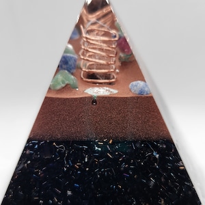 May include: A clear pyramid with a copper coil and various crystals inside. The base of the pyramid is layered with black and silver glitter.