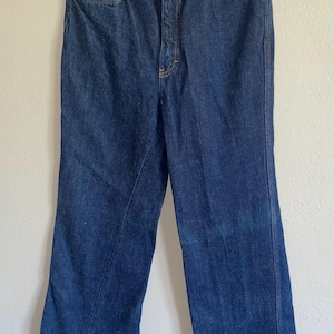 Può includere: Jeans di denim blu scuro con un classico design a cinque tasche. I jeans hanno un taglio dritto e una chiusura con bottone e cerniera. Il denim sembra essere di peso medio, adatto all'uso quotidiano.