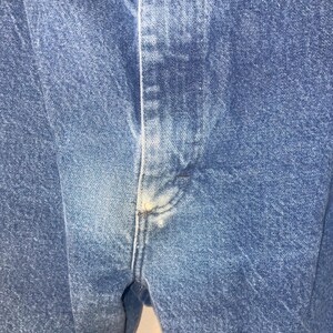 May include: Close-up of blue denim fabric with a visible seam down the centre.