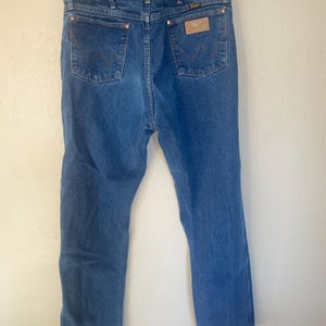 May include: A pair of blue denim jeans with a brown leather patch on the back pocket that says "Wrangler".